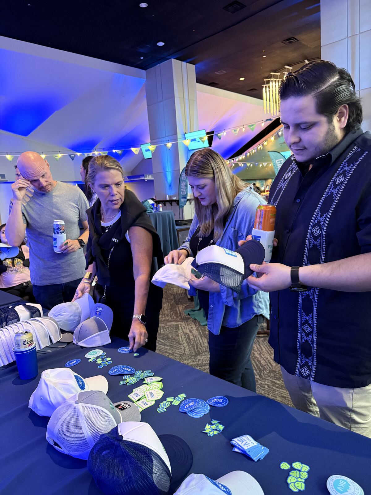 Four guests comparing cap styles and patch options at an evening company event