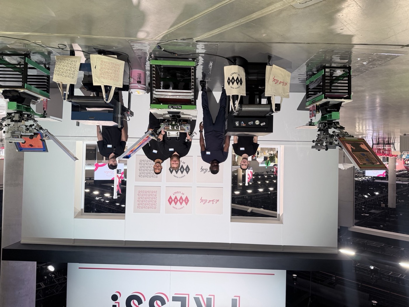 Merch Troop crew standing behind a row of presses and equipment at a convention activation